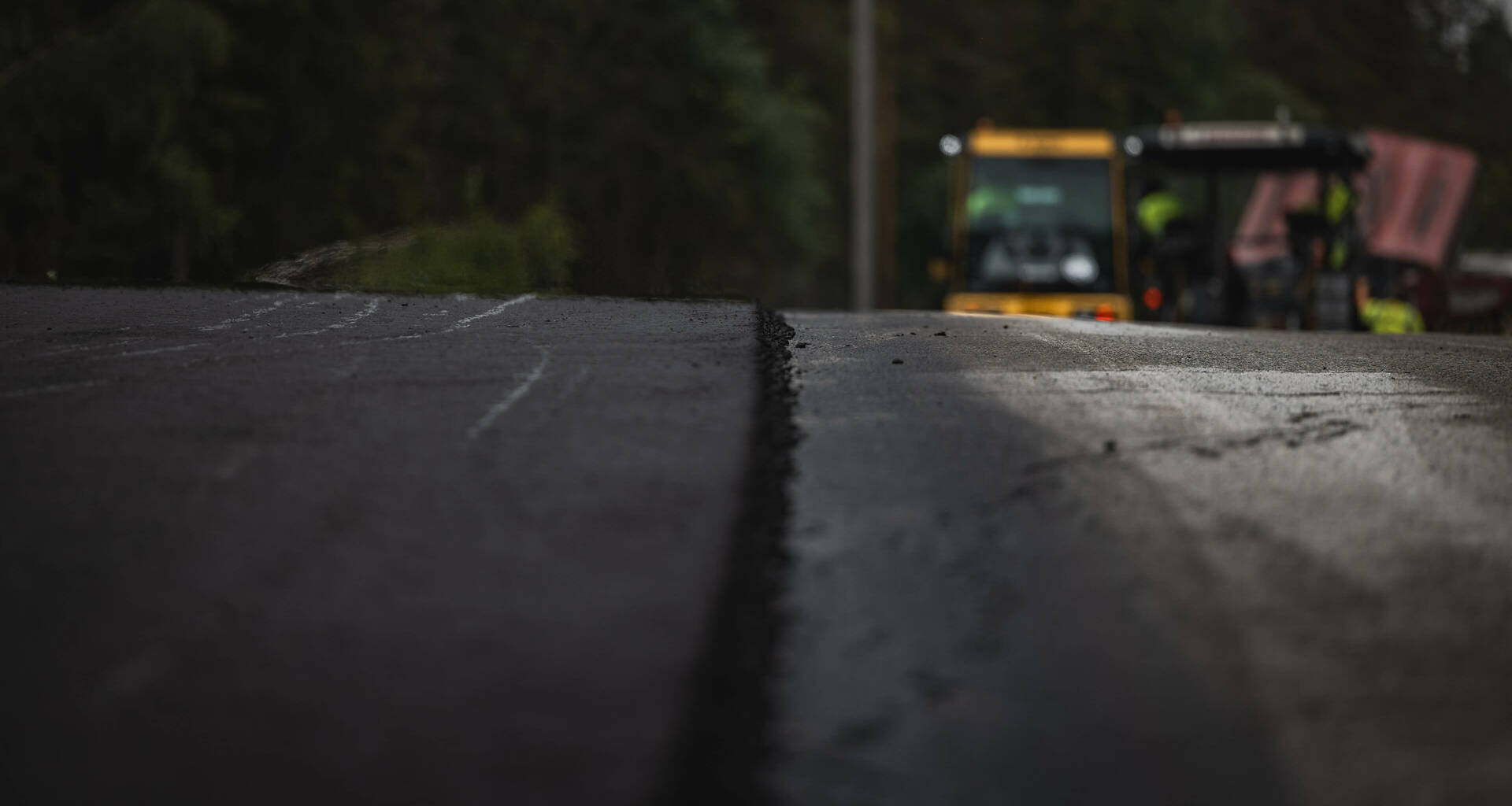 Nærbilde av nylagt asfalt med asfaltbil i bakgrunnen. Foto